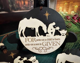 Puede incluir: Adorno navideño de madera negra y natural con un diseño recortado de escena de la natividad. El adorno presenta una estrella, una figura arrodillada, un camello y el texto "FOR unto us a child is born unto us a son is GIVEN".