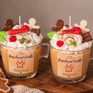 Puede incluir: Dos tazas de cristal rellenas de cera color canela, cubiertas con cera batida blanca, un hombre de jengibre marrón, uno blanco, un bastón de caramelo rojo, una hoja verde, una flor roja y un trozo de chocolate. Etiquetas: Lovely Candles Gingerbread Candle.