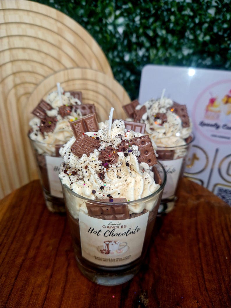 Puede incluir: Tres velas de cristal rellenas de cera marr&oacute;n oscuro, cubiertas con cera blanca batida que parece nata, decoradas con peque&ntilde;as piezas de cera con forma de tableta de chocolate y galleta, y espolvoreadas con purpurina. Etiqueta Hot Chocolate.