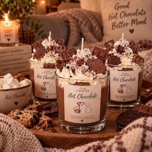 Puede incluir: Tres velas de cristal con forma de tazas de chocolate caliente, cubiertas con nata montada de cera blanca, trozos de chocolate y galletas. Cada etiqueta dice Lovely Candles Hot Chocolate, acompa&ntilde;ada de un peque&ntilde;o icono de coraz&oacute;n.