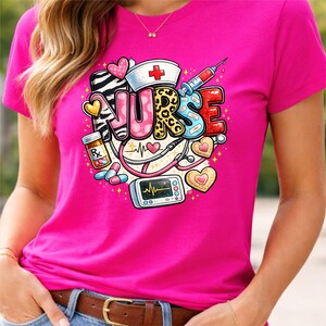 Op de afbeelding: Een felroze t-shirt met een kleurrijk grafisch ontwerp. Het ontwerp toont het woord "NURSE" in verschillende patronen en bevat een verpleegstershoed, een spuit, een stethoscoop en medische symbolen.