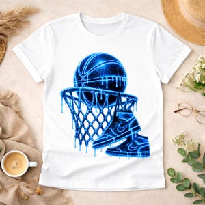 May include: A white short-sleeved t-shirt featuring a graphic print of a basketball and a basketball hoop with two high-top sneakers hanging from the rim. The entire design is rendered in a vibrant, glowing blue color with a dripping effect.