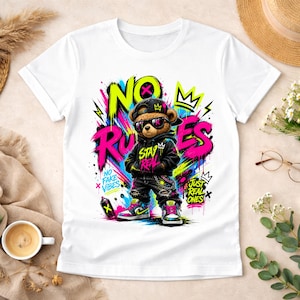 May include: White t-shirt featuring a graphic of a teddy bear wearing sunglasses, a cap, and a hoodie. The design includes the words "NO RULES" in bright colors, along with other text and graffiti-style elements.