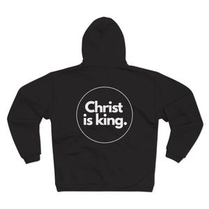Peut inclure: Sweat-shirt à capuche noir avec un cercle blanc au dos qui dit "Christ is king."