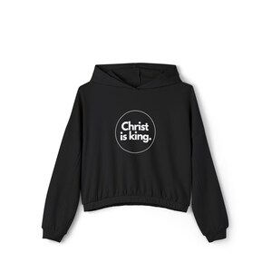 Könnte beinhalten: Schwarzer Kapuzenpullover mit dem weißen Text "Christ is king." in einem Kreis. Der Pullover hat lange Ärmel und einen Kordelzug in der Taille. Der Text ist fett und ohne Serifen.