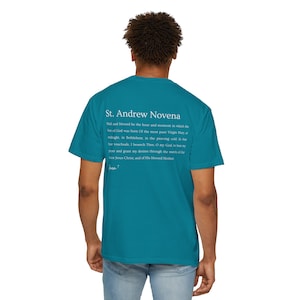May include: Teal blue t-shirt with white text that reads "St. Andrew Novena" and a prayer. The text includes the following: "Hall and blessed be the hour and moment in which the Son of God was born Of the most pure Virgin Mary, a midnight, in Bethlehem, in the piercing cold lathe In vouchsafe, I beseech. Then. O my God, zoer and grant my desires through the merm of Or vor Jesus Christ, and of His blessed Mother ent"