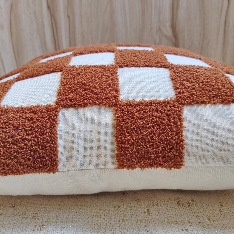 May include: A brown and white checkered throw pillow with a fluffy texture. The pillow is made of a soft, woven fabric.