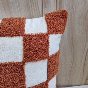 May include: A brown and white checkered throw pillow with a fluffy texture. The pillow is made of a soft, woven fabric.