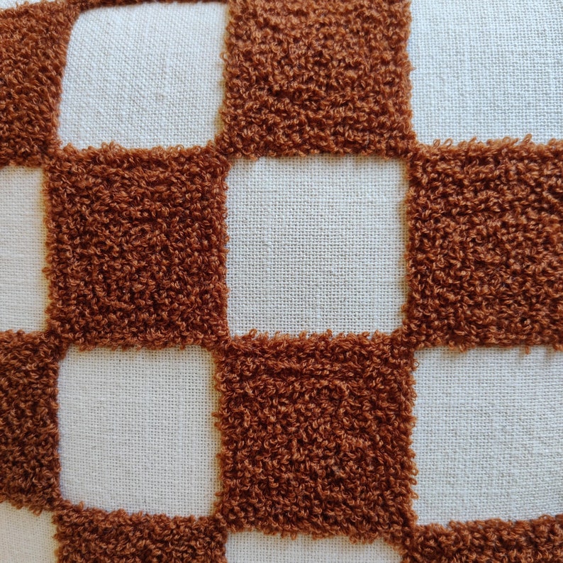 May include: A white pillow with a brown checkered pattern. The squares are made of a fluffy, textured fabric.