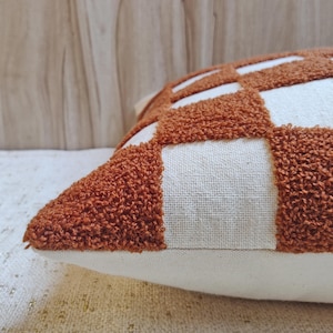 May include: A brown and white checkered throw pillow with a fluffy texture. The pillow is made of a soft, plush fabric and has a subtle geometric pattern.