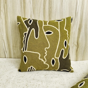 May include: A green cushion with a white and black abstract design. The design features stylised faces and lines.