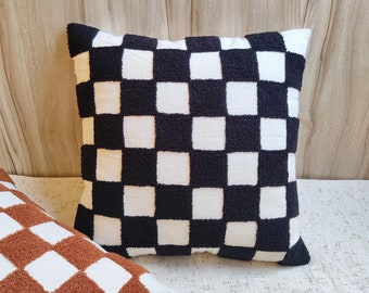 May include: Black and white checkered throw pillow with a fluffy texture. The pillow is made of a soft, woven fabric and has a square shape.