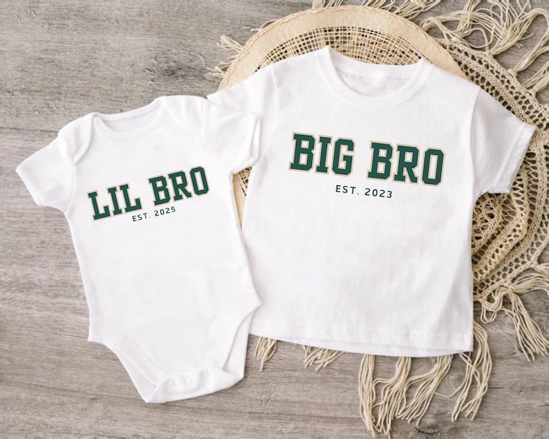 Puede incluir: Un body blanco de manga corta con el texto LIL BRO EST. 2025 en verde oscuro y una camiseta blanca de manga corta con el texto BIG BRO EST. 2023 en verde oscuro, ambos con letras de bloque y un fino contorno dorado.