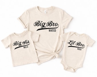 May include: Three beige t-shirts and a onesie with black script. The largest shirt says "Big Bro Mateo", the smaller shirt says "Big Sis Milla", and the onesie says "Lil Bro Noah". The shirts have short sleeves.