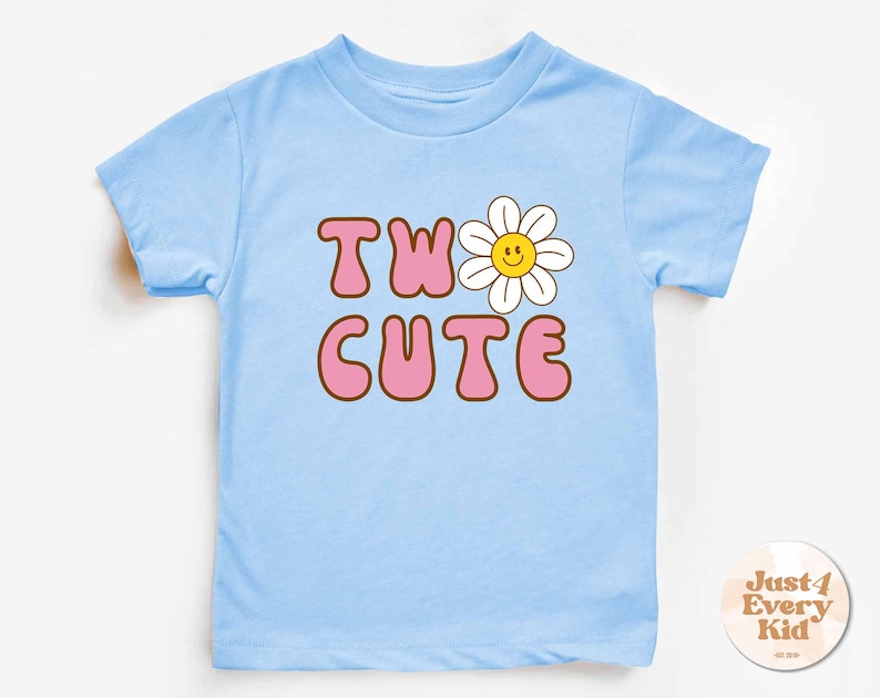May include: A light blue toddler t-shirt with the words "TWO CUTE" in pink bubble letters with a brown outline. A white daisy with a yellow smiling face replaces the "O" in "TWO". The shirt has short sleeves and a crew neck.