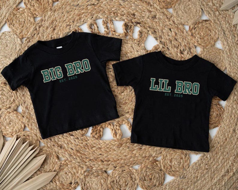 Puede incluir: Dos camisetas negras de manga corta. La camiseta de la izquierda tiene el texto en verde y blanco "BIG BRO EST. 2025". La camiseta de la derecha tiene el texto en verde y blanco "LIL BRO EST. 2025". Ambas tienen cuello redondo y dobladillo.
