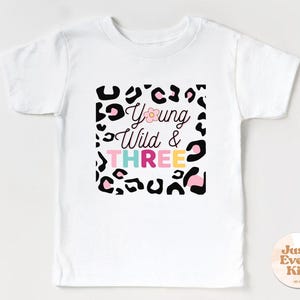 May include: White t-shirt with a leopard print design and the text "Young Wild & THREE" in pink, blue, and yellow letters.