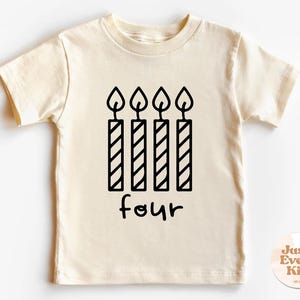 May include: A cream colored short-sleeved t-shirt with a black graphic of four candles and the word "four" written underneath. The shirt is for a child.