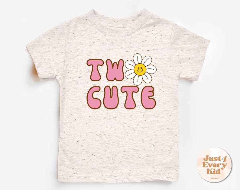 May include: A light gray t-shirt with the words "TWO CUTE" in pink bubble letters with a brown outline. A smiling daisy graphic is next to the word "TWO". The shirt has a round neck and short sleeves.