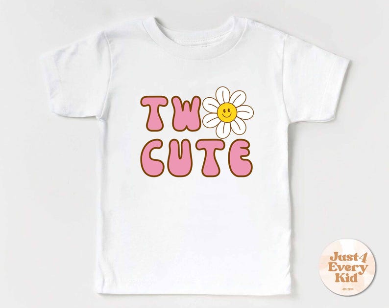 May include: White t-shirt with the words "TW0 CUTE" in pink bubble letters with a brown outline. A smiling daisy graphic is next to the word "TW0". The shirt has short sleeves and a round neck. A small circular logo is in the bottom right corner.