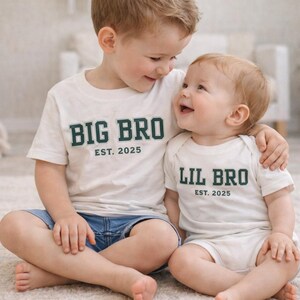 Puede incluir: Una camiseta blanca de manga corta con el texto verde oscuro BIG BRO EST. 2025 y un body blanco de manga corta con el texto verde oscuro LIL BRO EST. 2025. Ambas prendas cuentan con cuello redondo y un dise&ntilde;o sencillo y limpio.