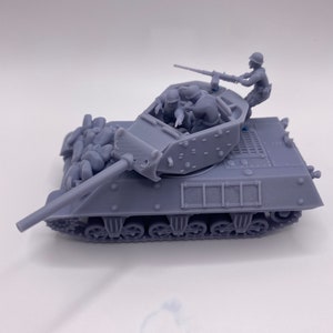 May include: A gray model of a military tank with a long barrel and a rotating turret. The tank has a detailed track system and is carrying several miniature soldiers. The tank is covered in a camouflage pattern.