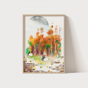 May include: A framed watercolor print featuring a serene autumn scene. The artwork depicts a forest with trees in shades of orange and red, two rabbits, and a large, gray moon. The print is in a light-colored wooden frame.
