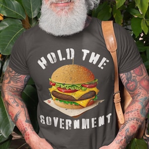 May include: A dark gray t-shirt with a white graphic of a hamburger and the text "Hold the Government".
