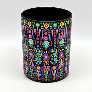 May include: A black cylindrical container with a vibrant, colorful pattern. The design features a repeating motif of circles, dots, and floral-like shapes in shades of red, orange, yellow, green, blue, and purple. The interior is black.