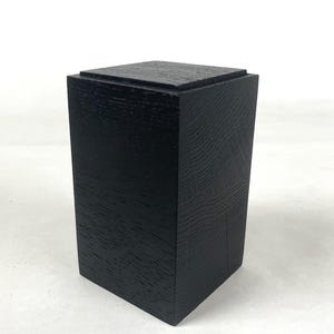 以下が含まれることがあります： 黒色の木製ボックス。表面はテクスチャ加工が施され、長方形で上部は正方形です。木目が確認できます。装飾品です。