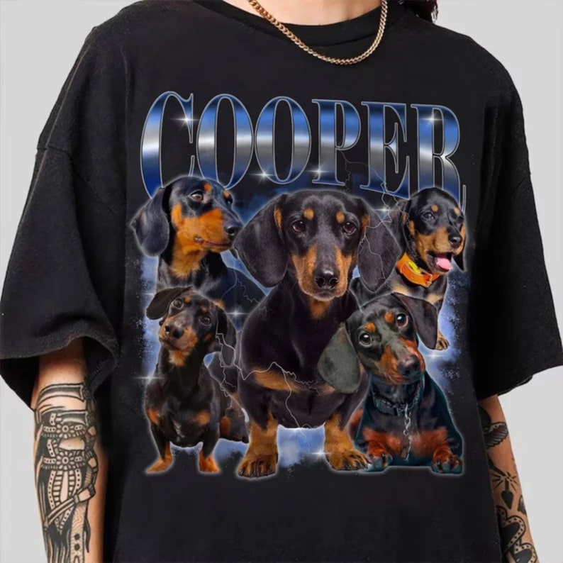 May include: A black t-shirt with a graphic print of five dachshund dogs. The dogs are arranged in a circle around the word "COOPER" in a blue and silver font.