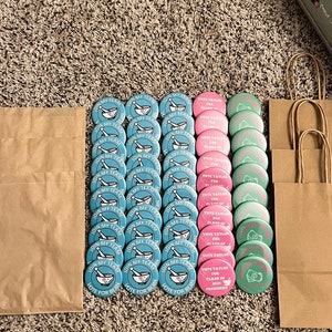 Puede incluir: Una colección de botones redondos azul verdoso y rosa con varios textos. Los botones están dispuestos en dos filas sobre una alfombra marrón. El texto en los botones azul verdoso dice "Join My Team" y "Vote for Bean". El texto en los botones rosas dice "Vote Taylor for Class of 2022 President".