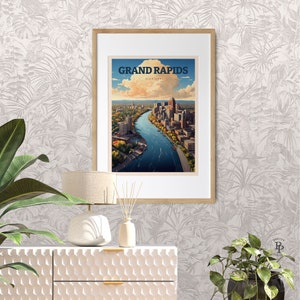 May include: A vintage-style travel poster featuring an aerial view of Grand Rapids, Michigan. The poster is framed in a light wood frame and is displayed on a white wall with a tropical leaf pattern.