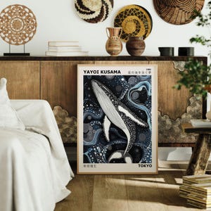 K&ouml;nnte beinhalten: Ein Poster mit einer Schwarz-Wei&szlig;-Illustration eines Wals, der in einem blauen und wei&szlig;en abstrakten Muster schwimmt. Das Poster tr&auml;gt den Titel "Yayoi Kusama" und "Das Meer der Punkte" in Japanisch. Das Poster ist gerahmt und h&auml;ngt an einer Wand.