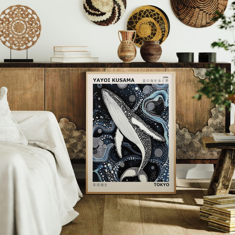 K&ouml;nnte beinhalten: Ein Poster mit einer Schwarz-Wei&szlig;-Illustration eines Wals, der in einem blauen und wei&szlig;en abstrakten Muster schwimmt. Das Poster tr&auml;gt den Titel "Yayoi Kusama" und "Das Meer der Punkte" in Japanisch. Das Poster ist gerahmt und h&auml;ngt an einer Wand.