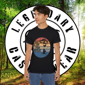 May include: A black t-shirt featuring a vintage-style graphic of a fisherman casting a line. The graphic has a sunset background with the text "Eat, Sleep, Fish, Repeat".