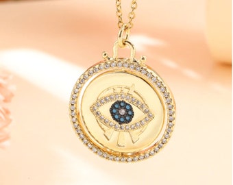 May include: Gold necklace with a spinning pendant featuring a blue evil eye with black and white accents surrounded by clear rhinestones.