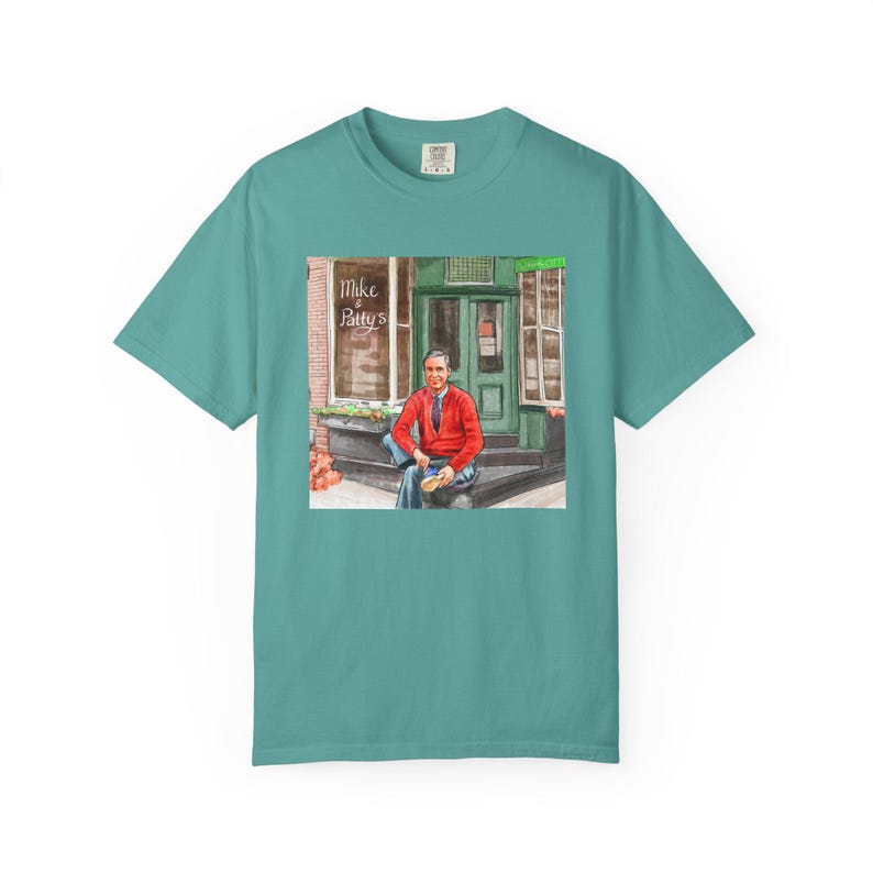 Illustrazione di un ritratto di Mr. Rogers seduto fuori da un bar, scena di strada, stampata su una maglietta. immagine 8