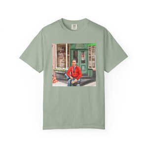 Illustrazione di un ritratto di Mr. Rogers seduto fuori da un bar, scena di strada, stampata su una maglietta. immagine 6