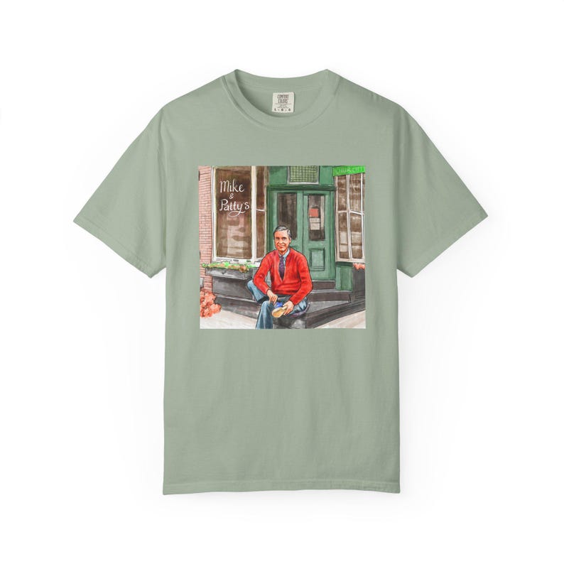 Illustrazione di un ritratto di Mr. Rogers seduto fuori da un bar, scena di strada, stampata su una maglietta. immagine 6