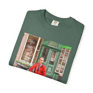 Illustrazione di un ritratto di Mr. Rogers seduto fuori da un bar, scena di strada, stampata su una maglietta. immagine 15