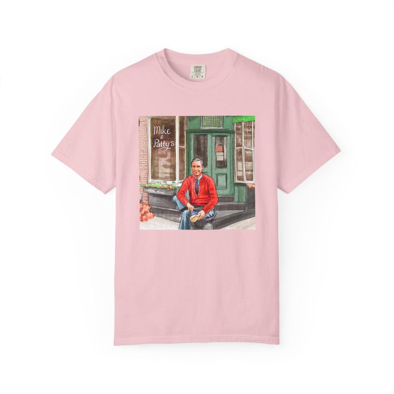Illustrazione di un ritratto di Mr. Rogers seduto fuori da un bar, scena di strada, stampata su una maglietta. immagine 11