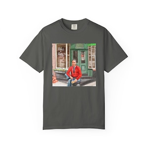Illustrazione di un ritratto di Mr. Rogers seduto fuori da un bar, scena di strada, stampata su una maglietta. immagine 4