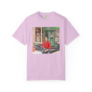 Illustrazione di un ritratto di Mr. Rogers seduto fuori da un bar, scena di strada, stampata su una maglietta. immagine 10