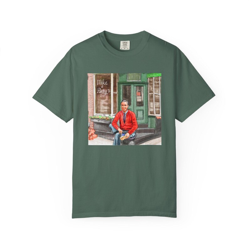 Illustrazione di un ritratto di Mr. Rogers seduto fuori da un bar, scena di strada, stampata su una maglietta. immagine 7