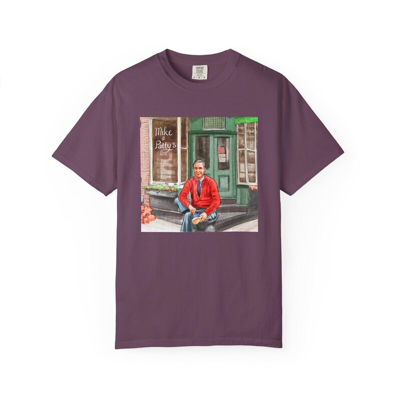 Illustrazione di un ritratto di Mr. Rogers seduto fuori da un bar, scena di strada, stampata su una maglietta. immagine 12