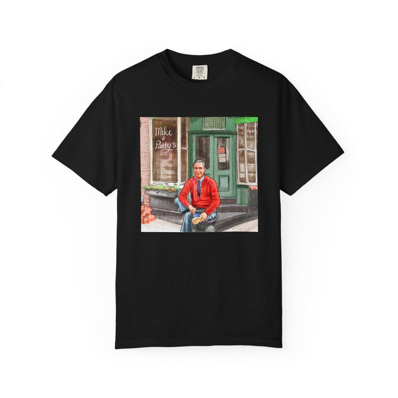 Illustrazione di un ritratto di Mr. Rogers seduto fuori da un bar, scena di strada, stampata su una maglietta. immagine 9