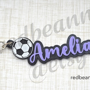 May include: A black and purple personalized keychain with the name "Amelia" and a soccer ball charm.
