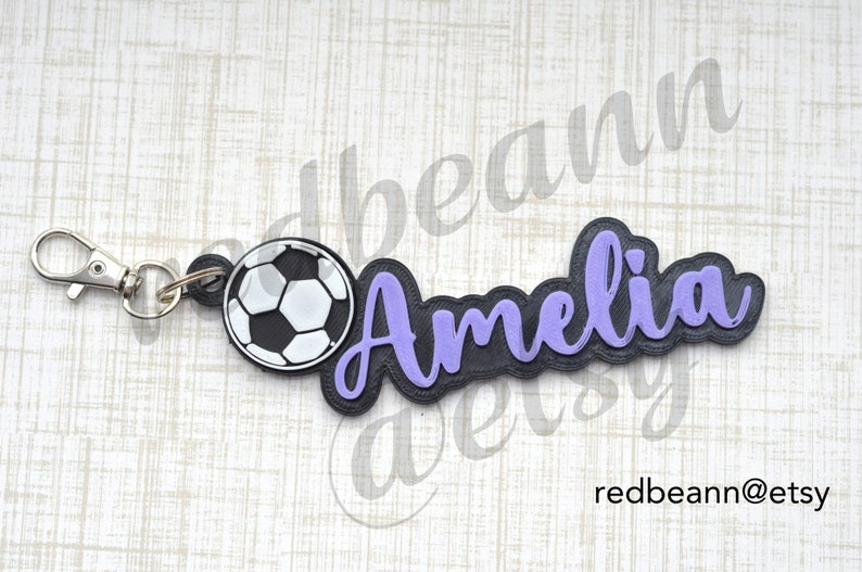 May include: A black and purple personalized keychain with the name "Amelia" and a soccer ball charm.