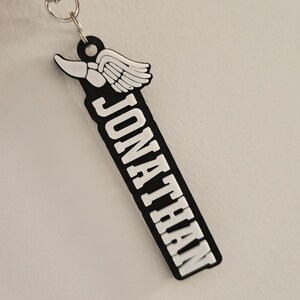 May include: Black and white keychain with the name "JONATHAN" in white lettering and a white winged foot design.